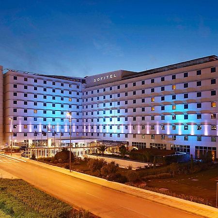 雅典索菲特机场酒店 Spáta 外观 照片 The photo shows a large modern hotel building, likely named "Sofitel," illuminated with blue and purple lights as evening approaches. The structure features multiple floors and a contemporary design, with large windows and a flat facade. In front of 