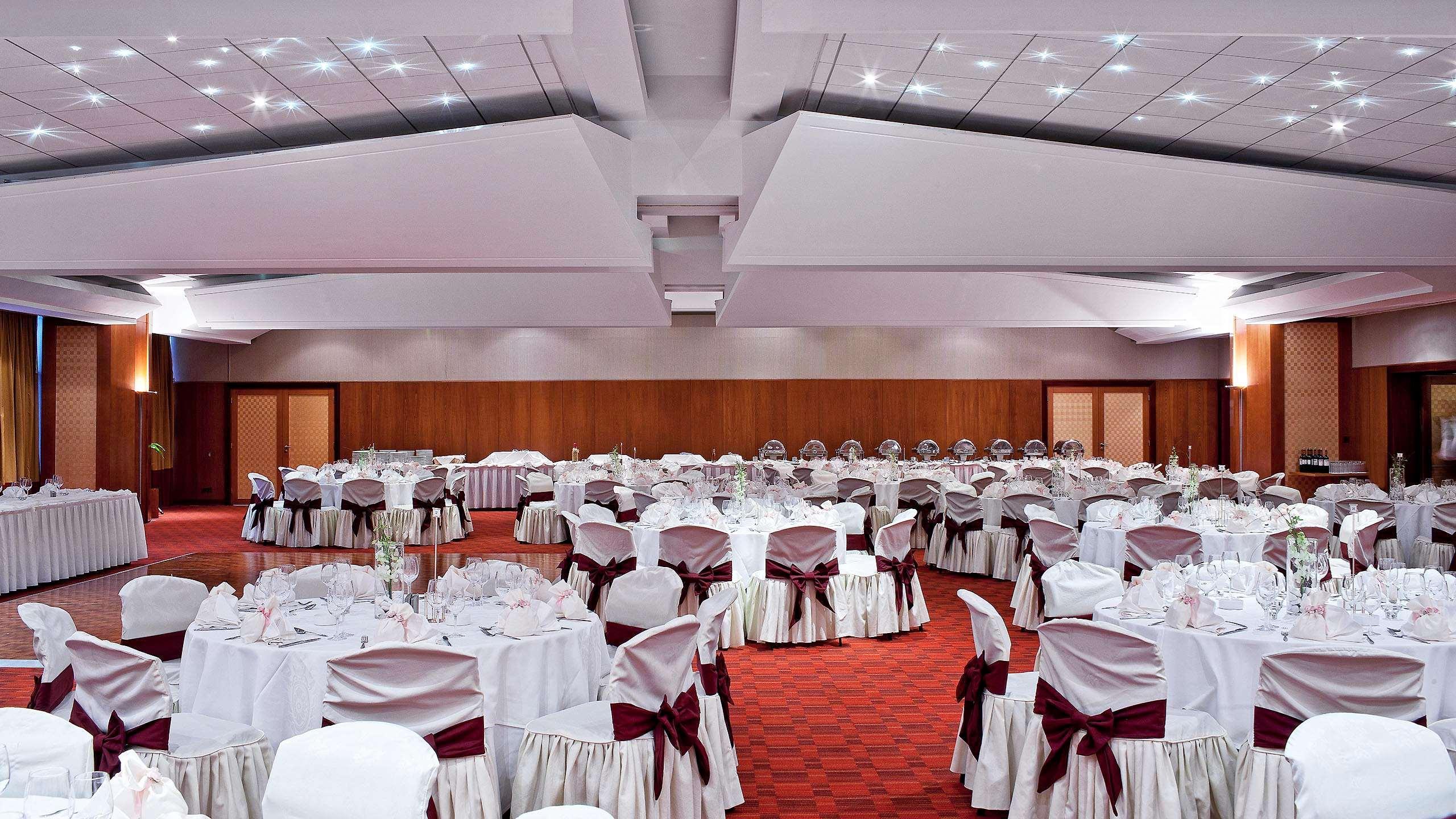 雅典索菲特机场酒店 Spáta 外观 照片 The photo shows an elegantly arranged banquet hall. The space features numerous round tables, each covered with white tablecloths and adorned with deep red sashes around the chairs. The flooring is carpeted in a rich red, and the walls are a warm woo