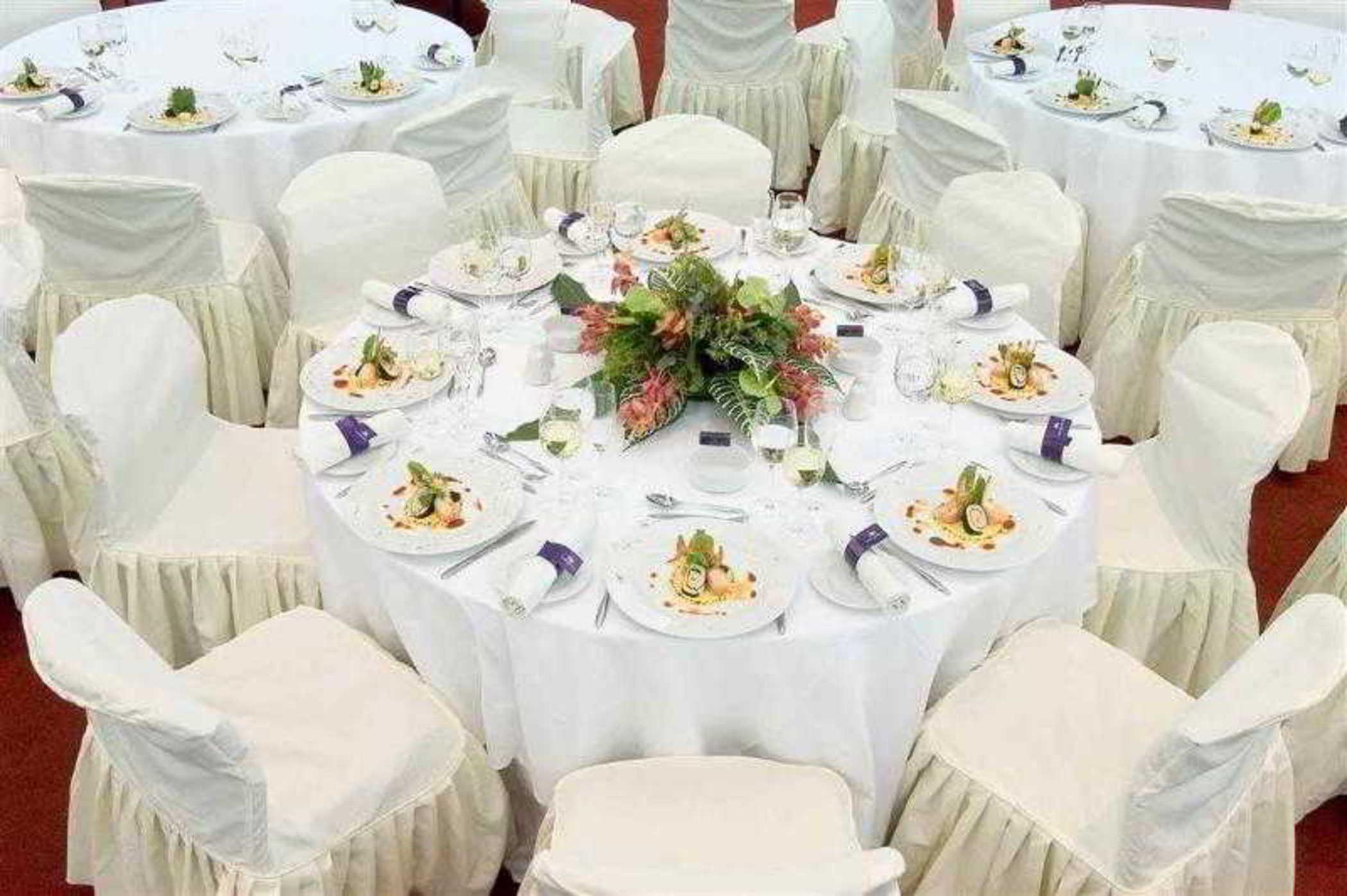 雅典索菲特机场酒店 Spáta 外观 照片 The image shows a beautifully arranged dining setup. There are several round tables covered with white tablecloths, and each table is surrounded by white chairs, likely dressed in covers that drape to the ground. 

On each table, there are elegant pl