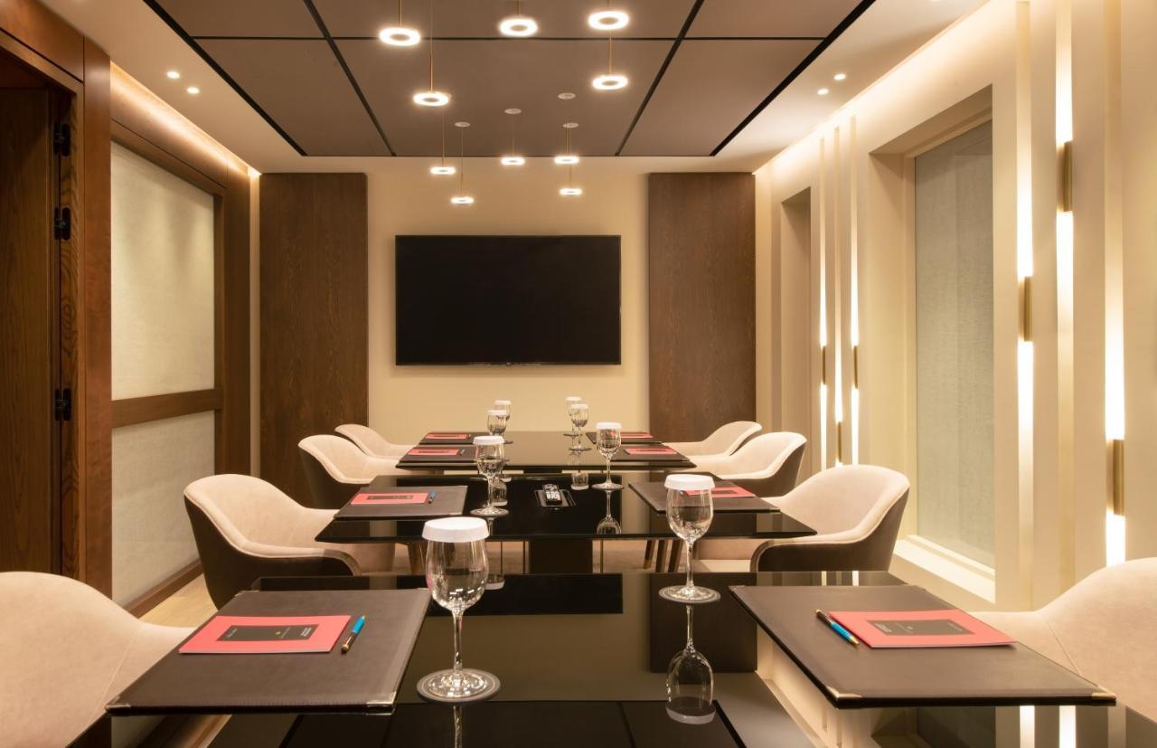 雅典索菲特机场酒店 Spáta 外观 照片 The photo depicts a modern conference room. It features a sleek glass table surrounded by stylish chairs. Each place setting includes a glass of water and a menu or notepad. The room is well-lit with recessed lighting and has a large flat-screen tele