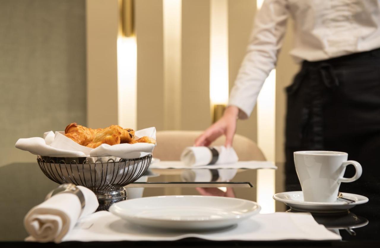 雅典索菲特机场酒店 Spáta 外观 照片 The photo shows a dining table setting in a restaurant. On the table, there is a white plate, a small cup, and a silver bowl containing pastries, likely croissants. The surrounding area has a clean, modern aesthetic with soft lighting. In the backgro