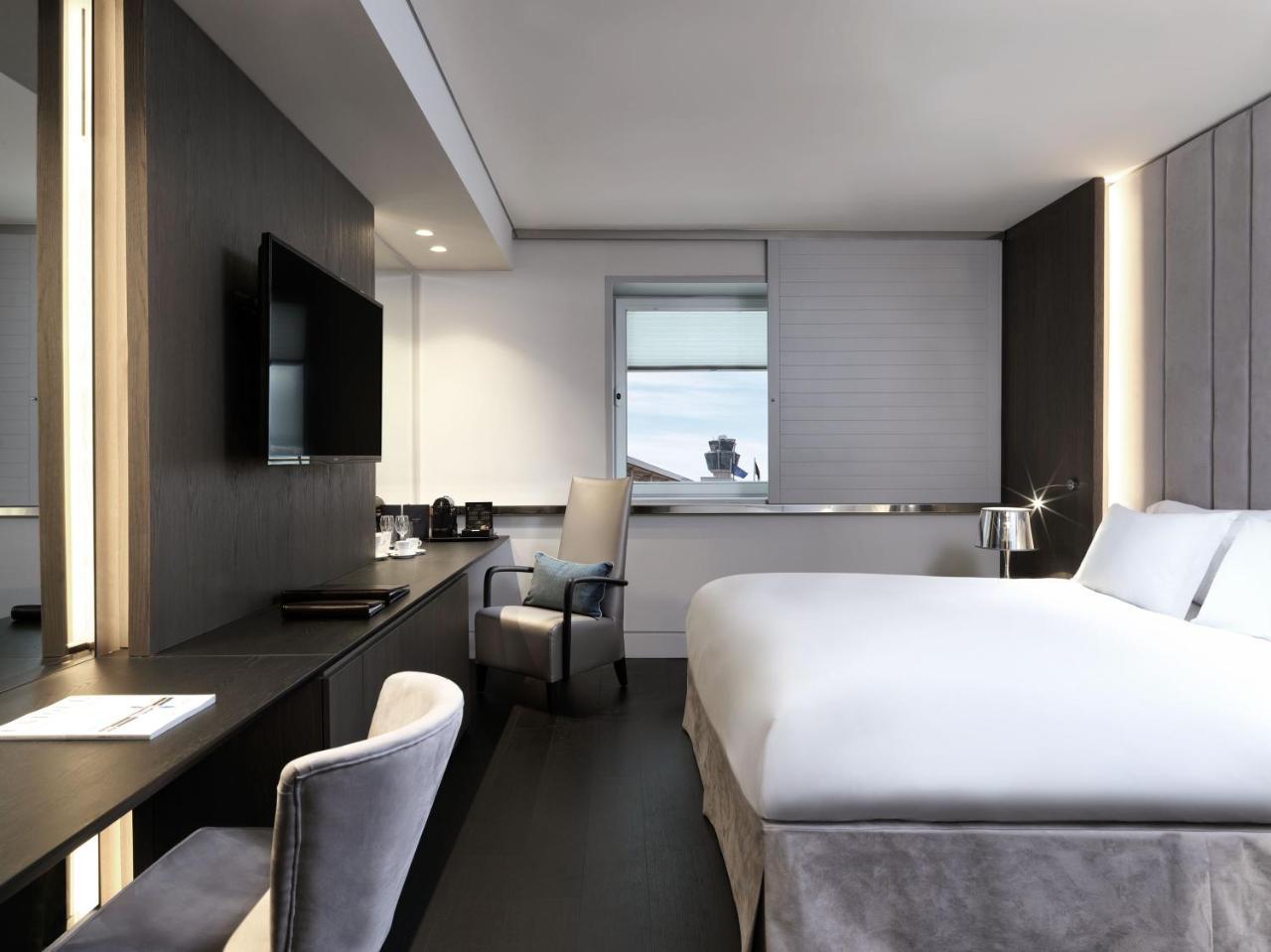 雅典索菲特机场酒店 Spáta 外观 照片 The photo shows a modern hotel room. It features a large bed with white bedding, a sleek desk with a chair, and a flat-screen TV mounted on the wall. There are large windows allowing natural light to enter, and the room is decorated in neutral tones 